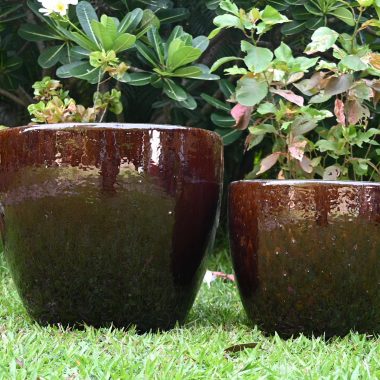 Glossy brown ceramic planters in a garden on green grass.