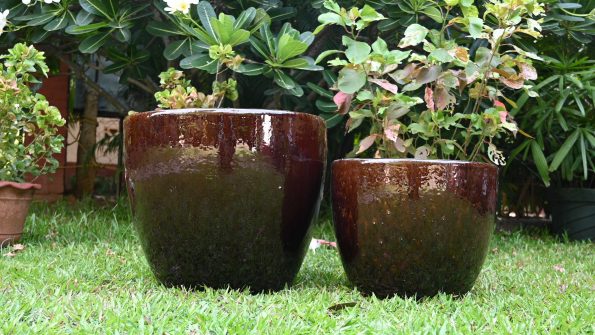 Glossy brown ceramic planters in a garden on green grass.