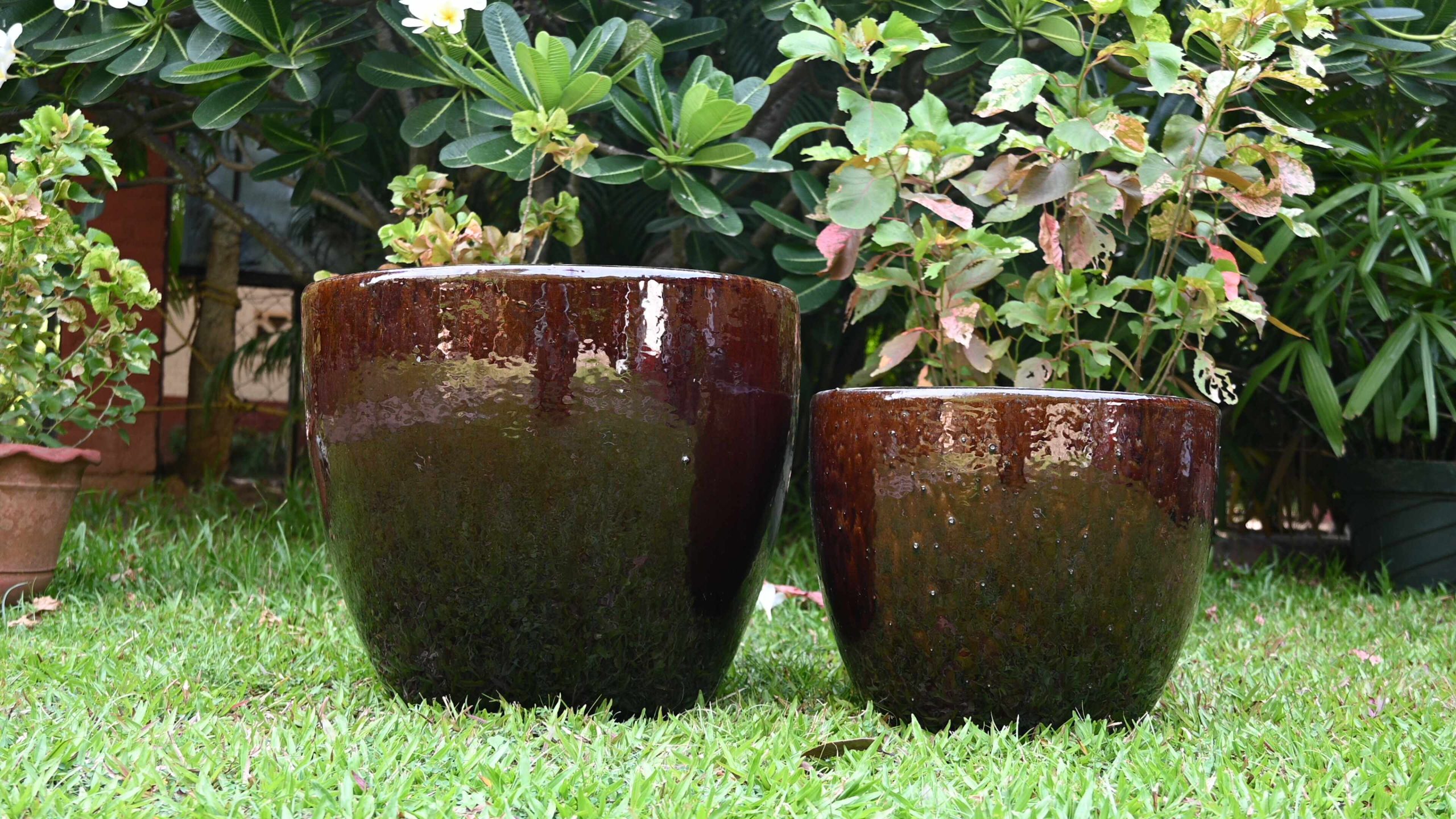 Glossy brown ceramic planters in a garden on green grass.