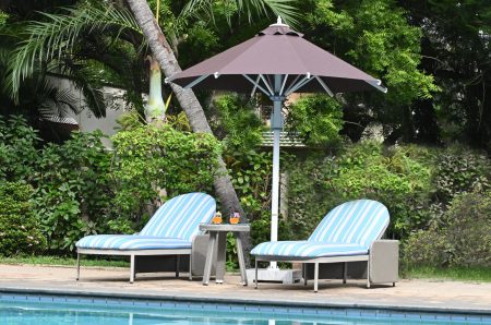 Poolside loungers with striped cushions in a lush garden under an umbrella