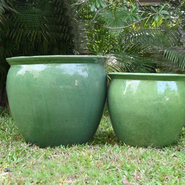 Two large green outdoor ceramic pots placed on grass with lush greenery in the background.