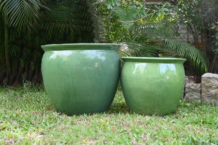 Two large green outdoor ceramic pots placed on grass with lush greenery in the background.