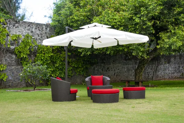Outdoor furniture in Bangalore garden with wicker chairs, red cushions, and umbrella shade.